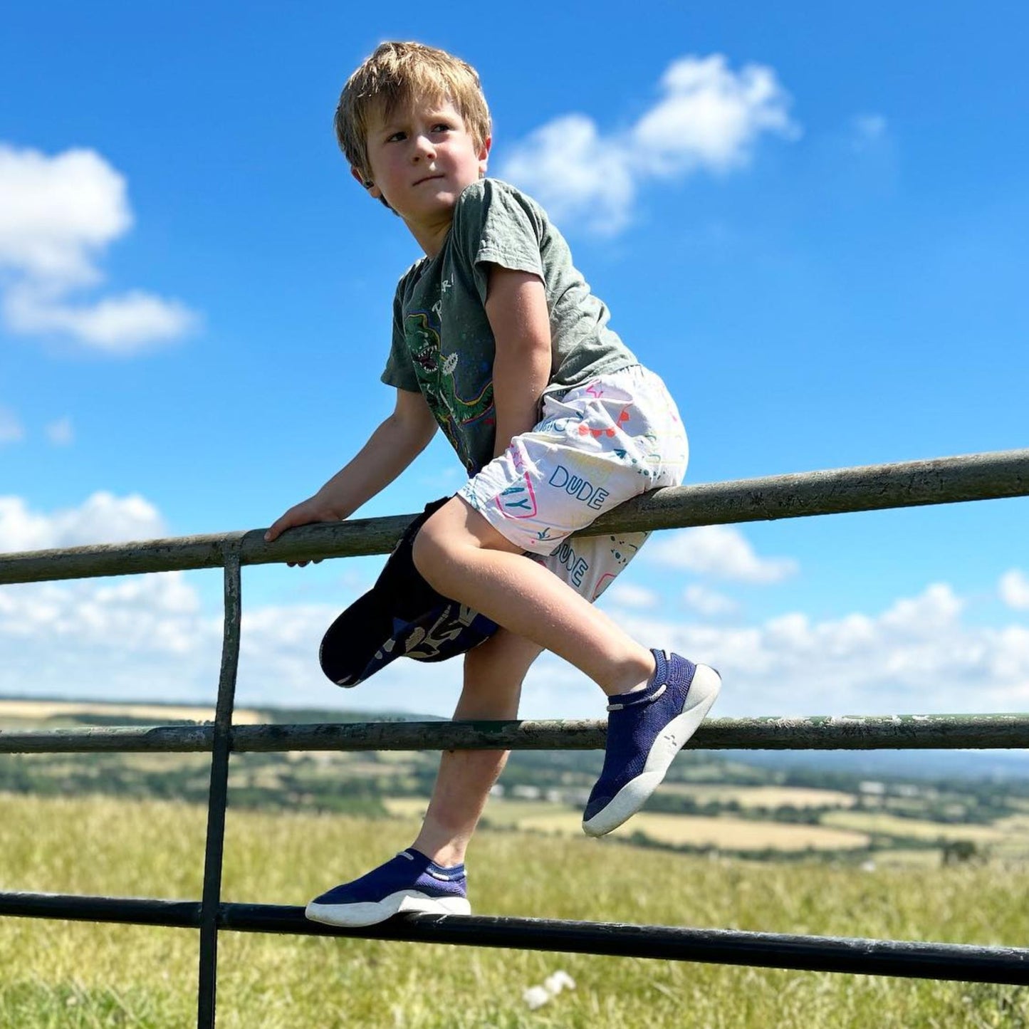 boy climbing gate wearing blue sustainable trainers